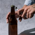 Close-up of hands using a lighter to open a craft beer bottle, shot in a studio setting.