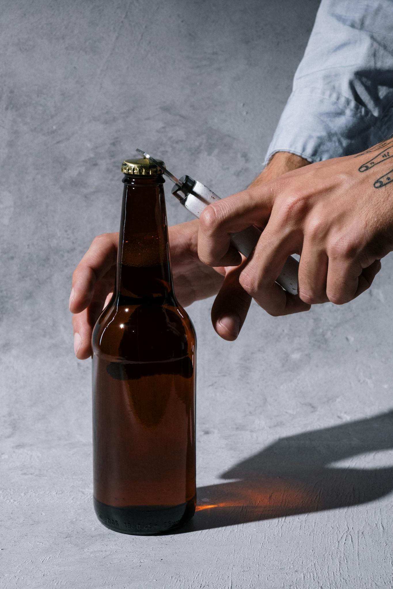 Close-up of hands using a lighter to open a craft beer bottle, shot in a studio setting.