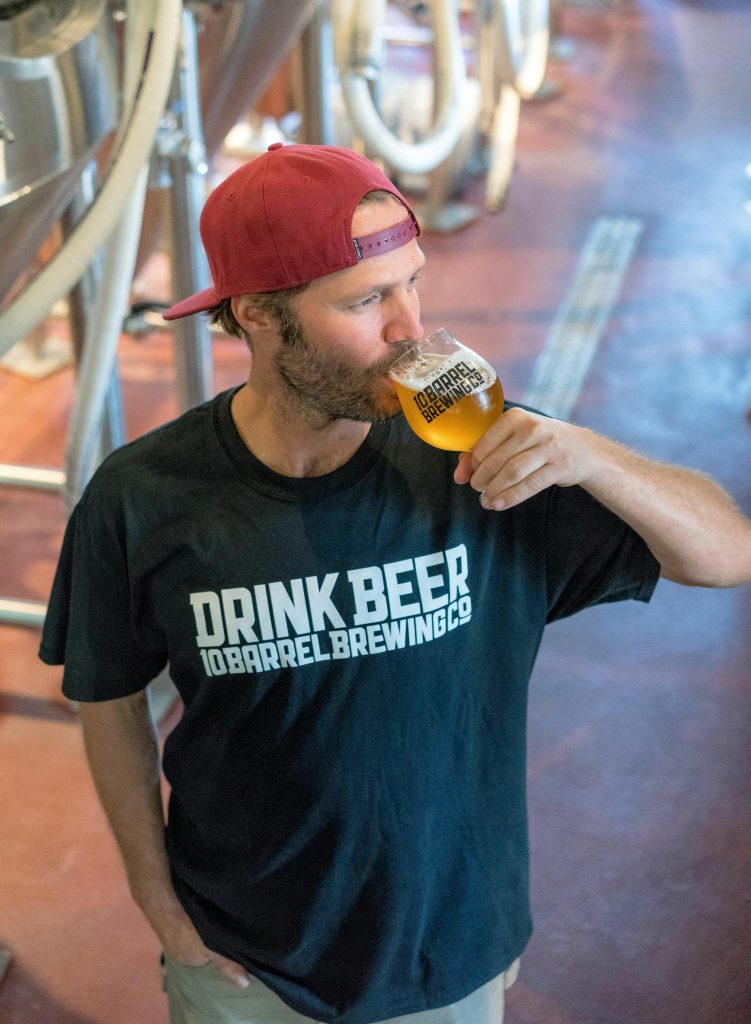 Man in black t-shirt and red cap drinking craft beer at a brewery.